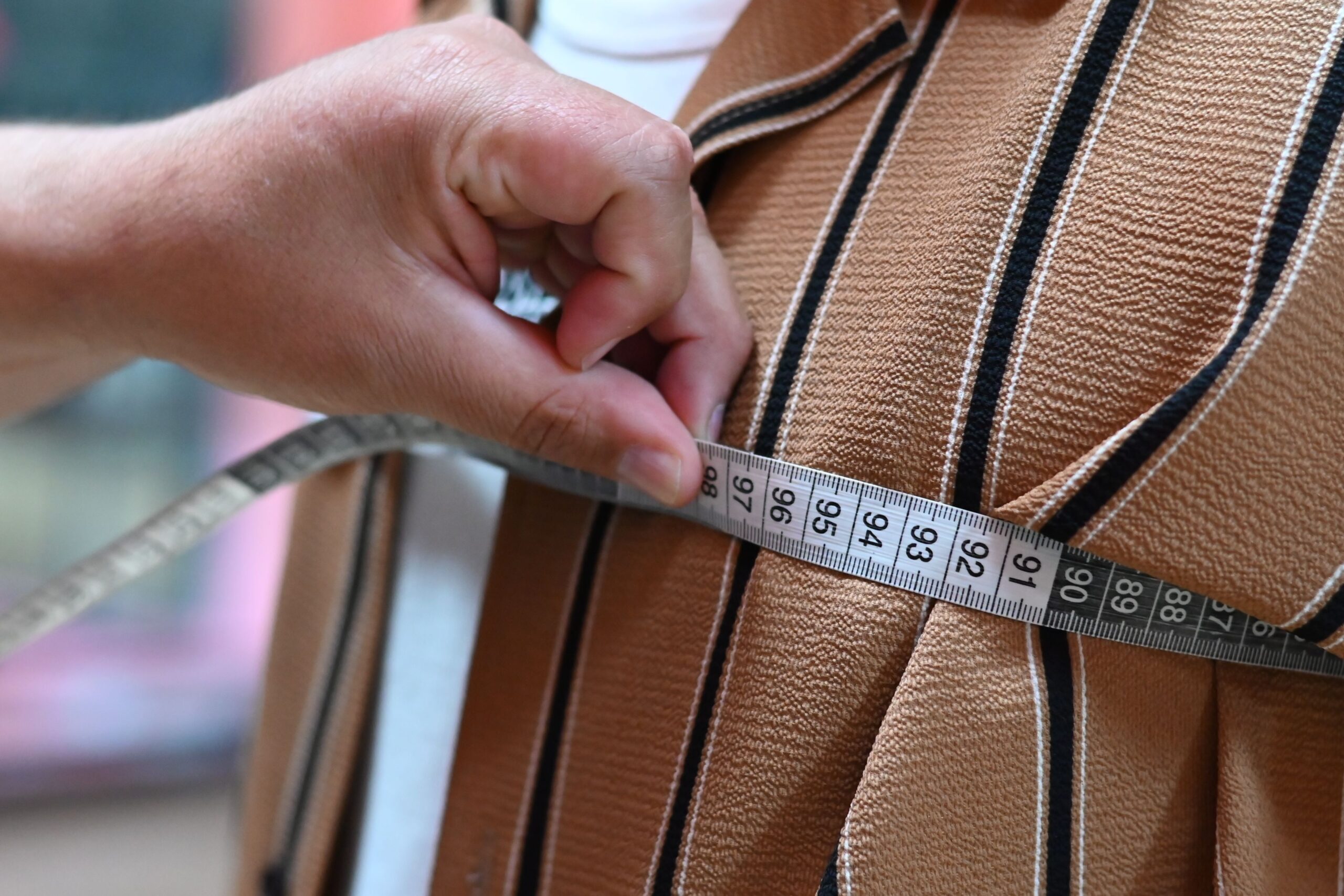 A close-up of a tailor measuring fabric with a tape, showcasing precision and craftsmanship.